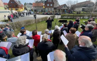 Chorgemeinschaft Reinhardtsdorf-Schöna e.V. - Ostersingen im Park 2023 - der Chor auf dem österlich geschmückten Dorfplatz mit Zuhörern