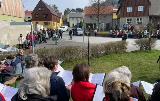 Chorgemeinschaft Reinhardtsdorf-Schöna e.V. - Ostersingen im Park 2023 - der Chor auf dem österlich geschmückten Dorfplatz mit Zuhörern