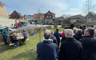 Chorgemeinschaft Reinhardtsdorf-Schöna e.V. - Ostersingen im Park 2023 - der Chor auf dem österlich geschmückten Dorfplatz mit Zuhörern und Bastelecke